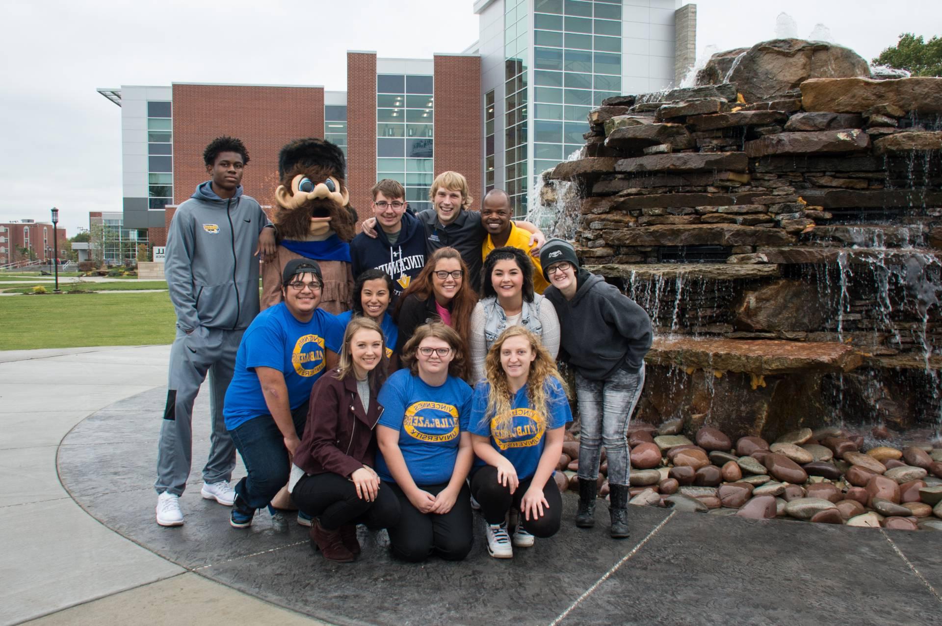 A group of students adn Trailblazer Willy are near the fountain at Updike